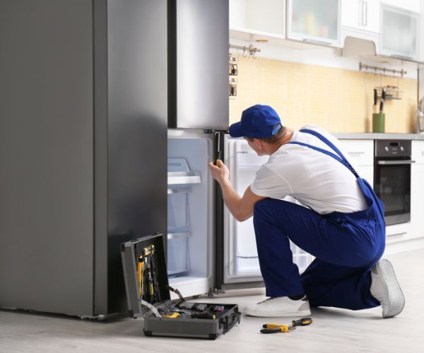 A man is working on a refrigerator in a kitchen.