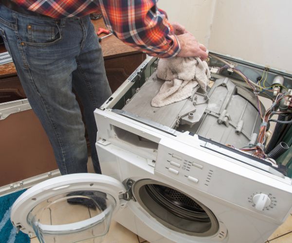 A man in a plaid shirt is working on a washing machine