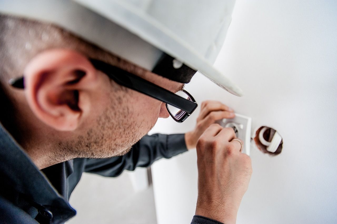 A man wearing a hard hat and glasses is working on an electrical outlet.