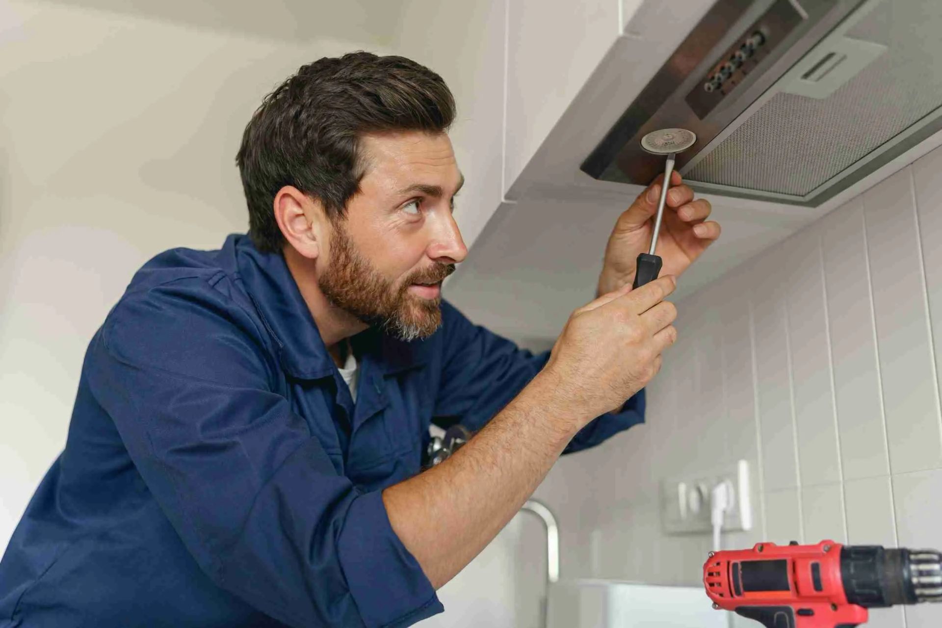 A man is fixing a kitchen hood with a screwdriver.