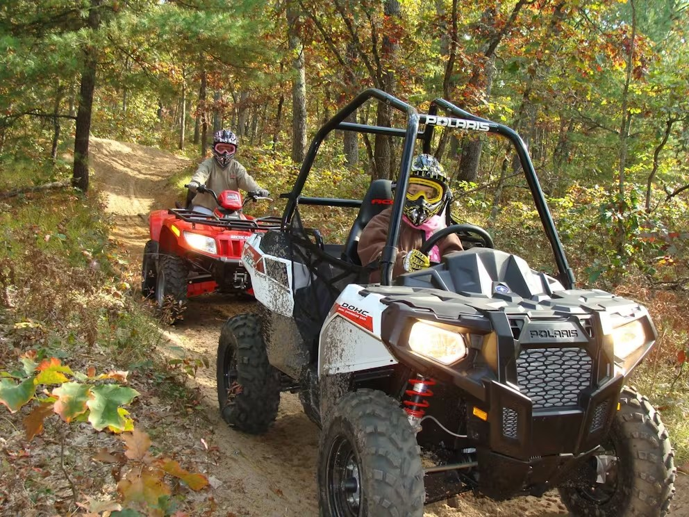 Two people are riding atvs on a trail in the woods.