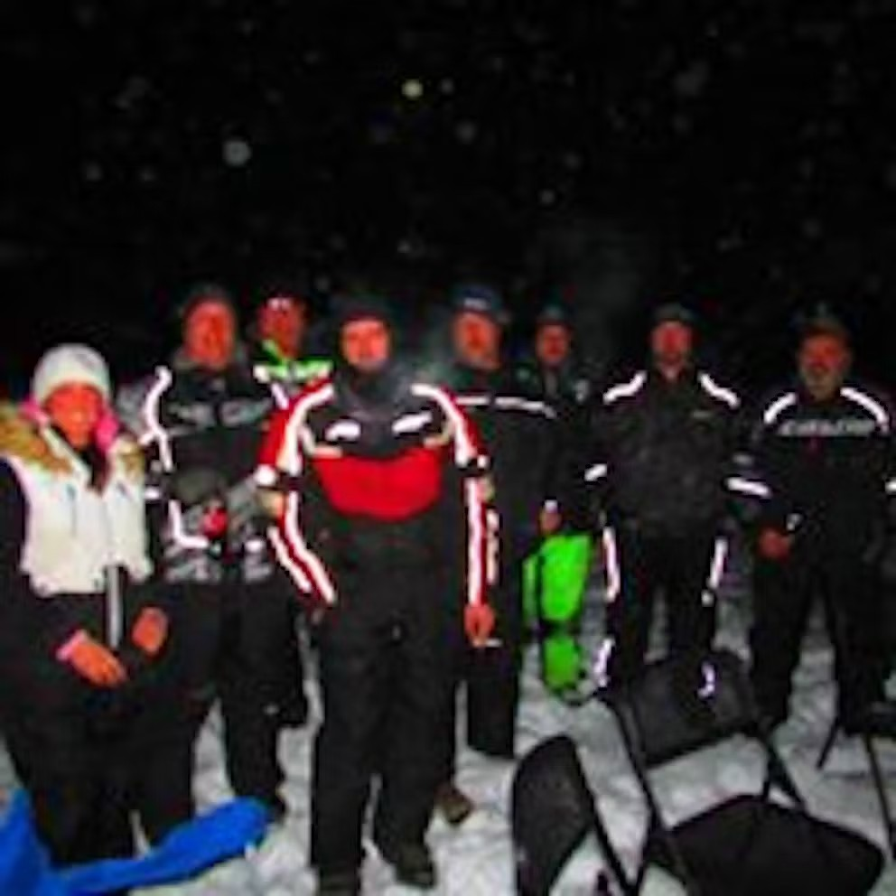 A group of people are standing in the snow at night.