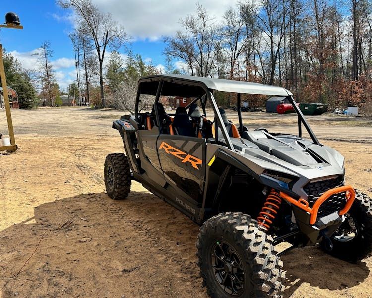A polaris rzr 1000 is parked in a dirt lot.