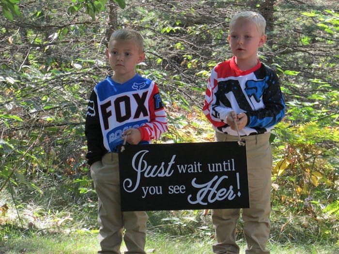 Two young boys holding a sign that says just wait until you see her