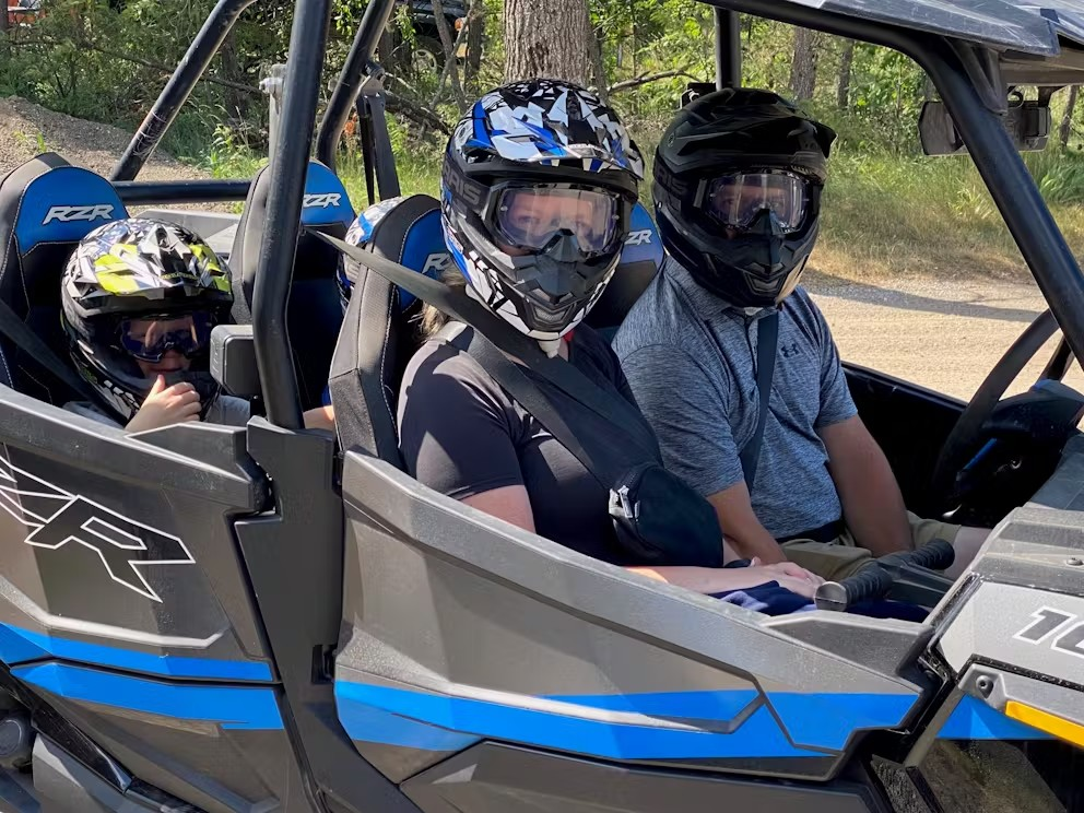 Two people are sitting in a atv wearing helmets.