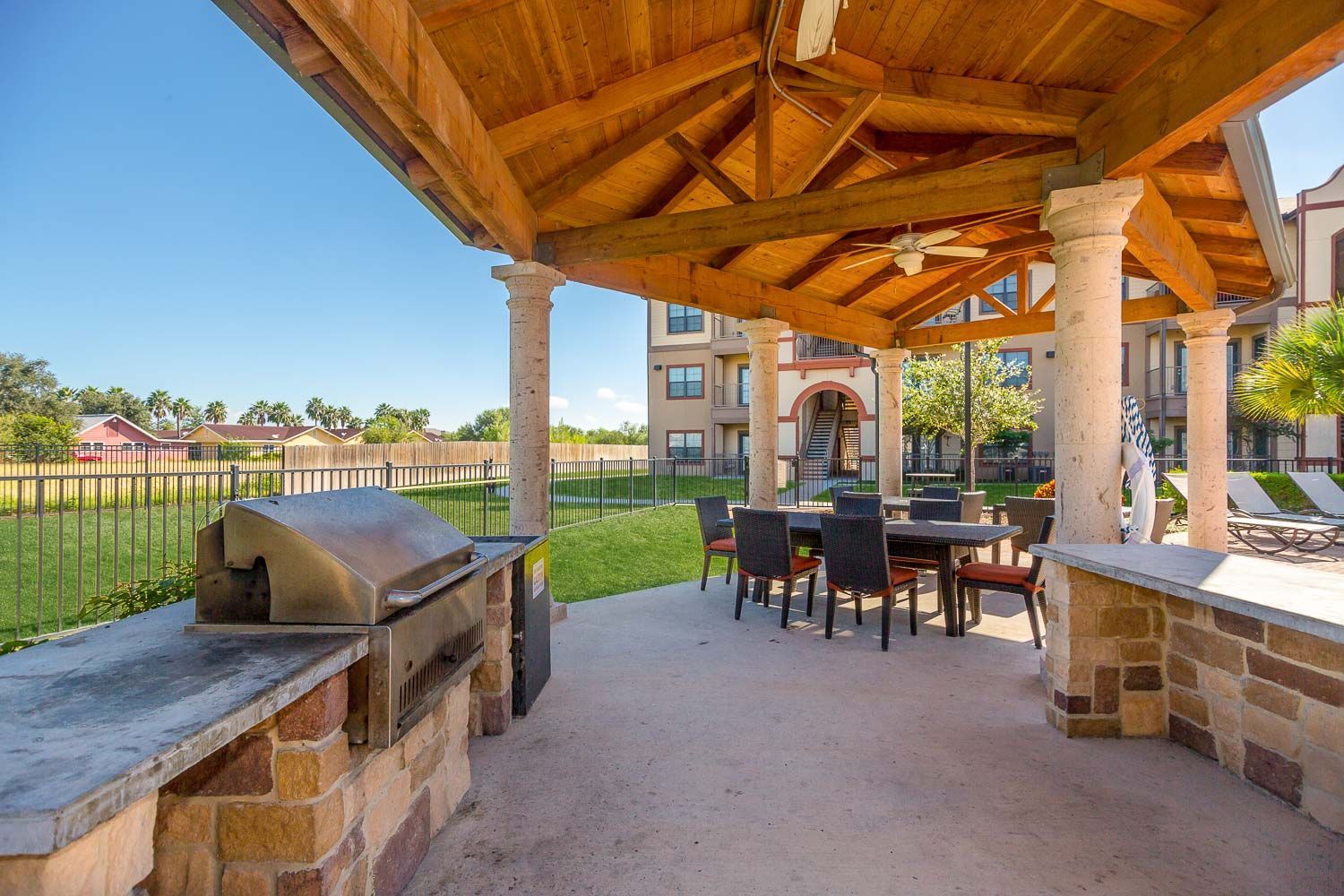 A covered patio with a grill and a table and chairs under a wooden roof.