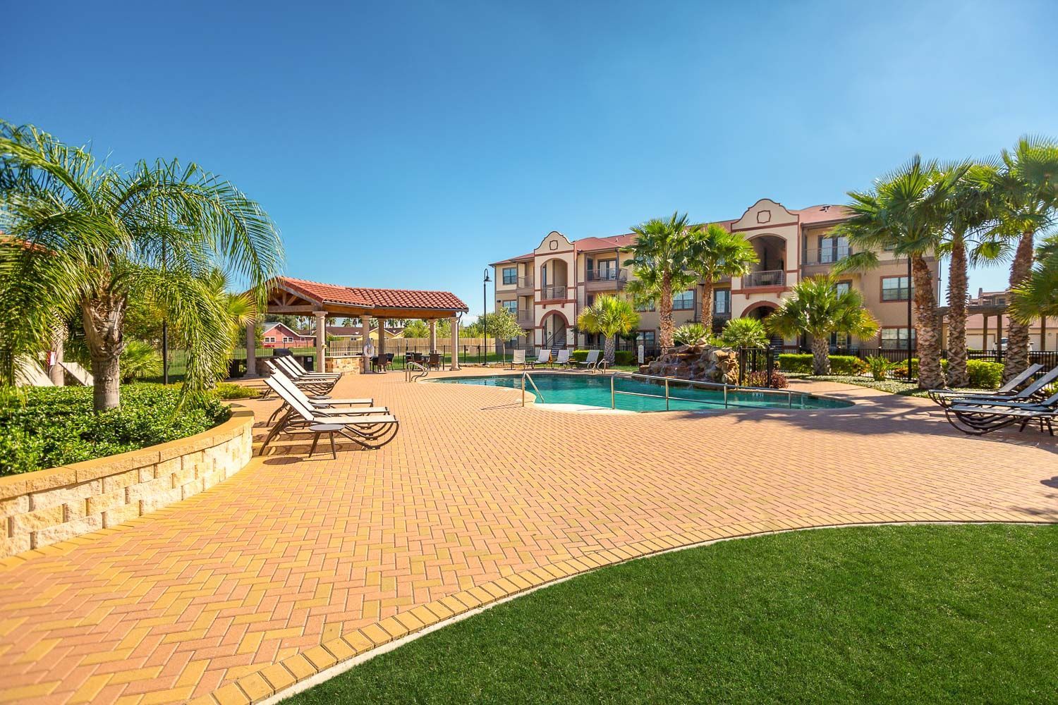 A large swimming pool surrounded by chairs and palm trees in front of a large building.