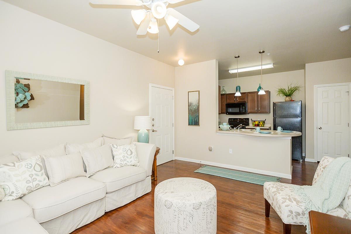 A living room with a couch , chair , ottoman and ceiling fan.