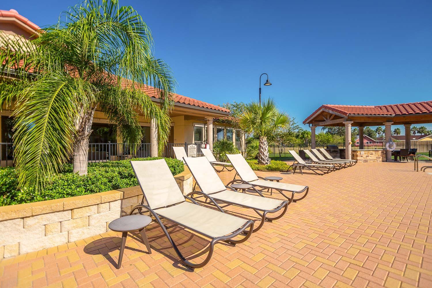 A row of lounge chairs are sitting on a brick patio next to a building.