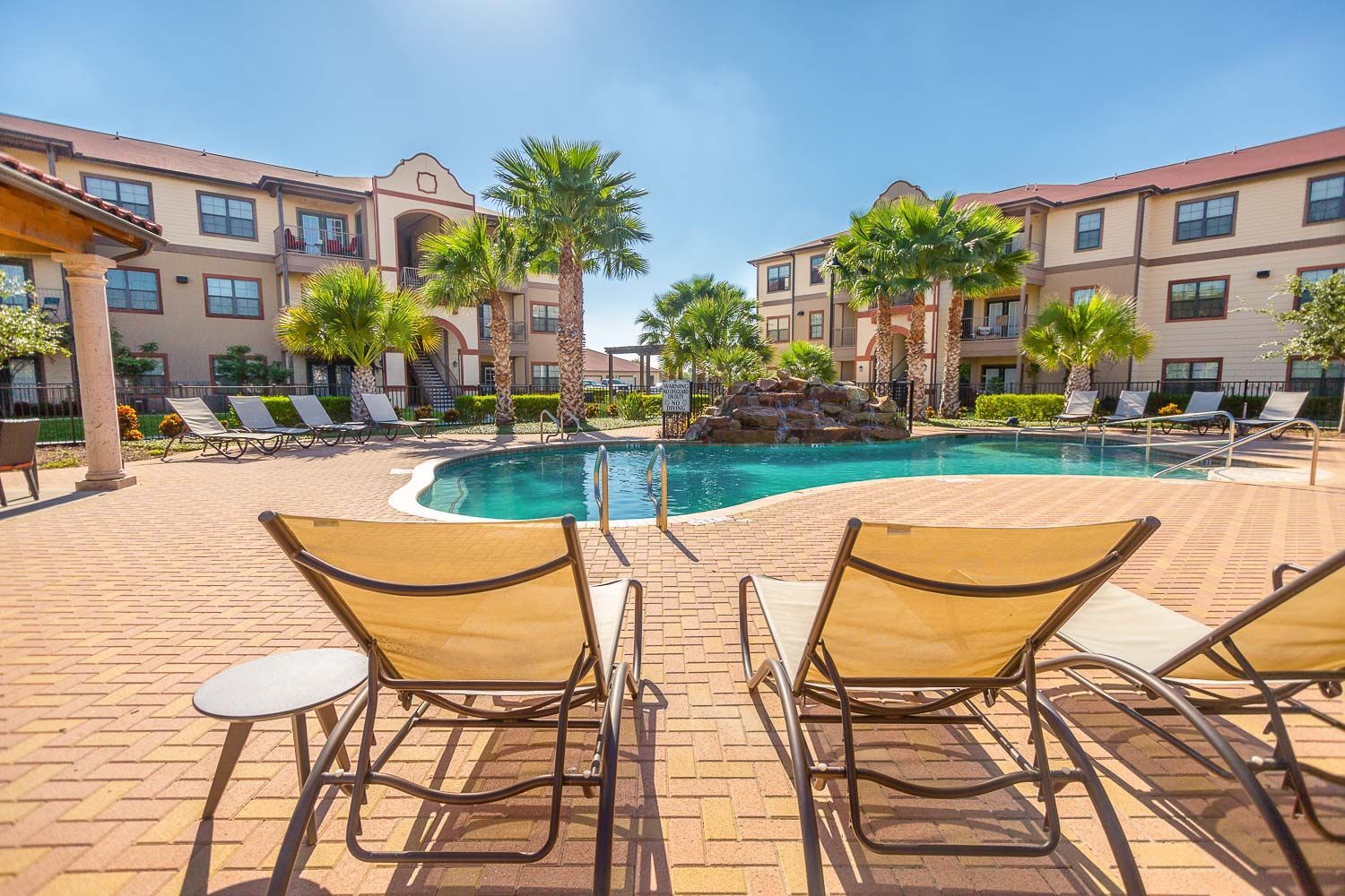 Two lounge chairs are sitting next to a large swimming pool in front of a building.