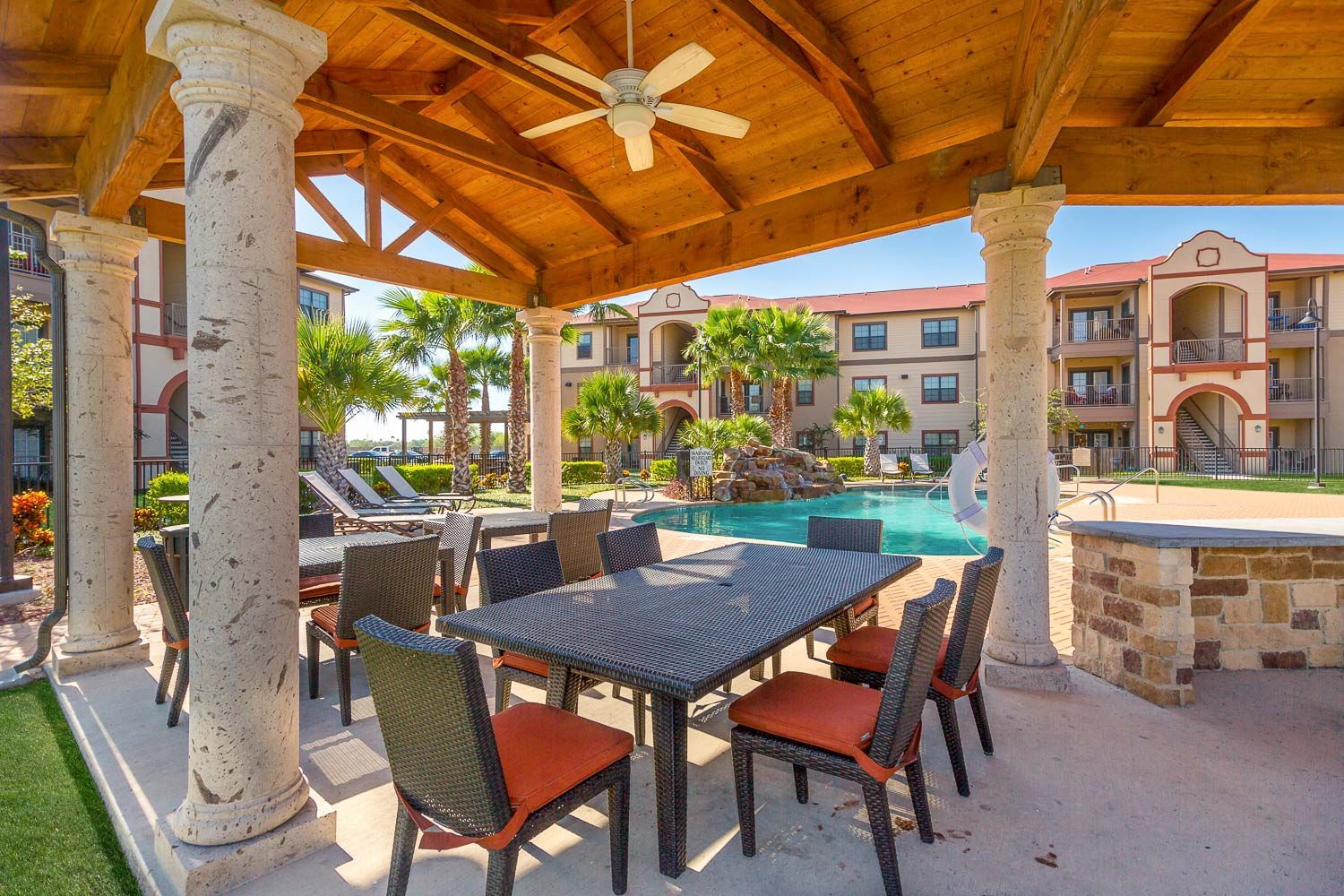 A patio area with a table and chairs under a canopy overlooking a pool.