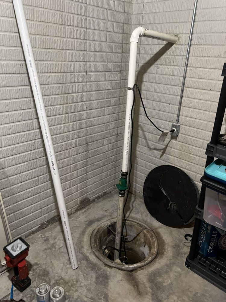 A basement with a sump pump in it and a brick wall.