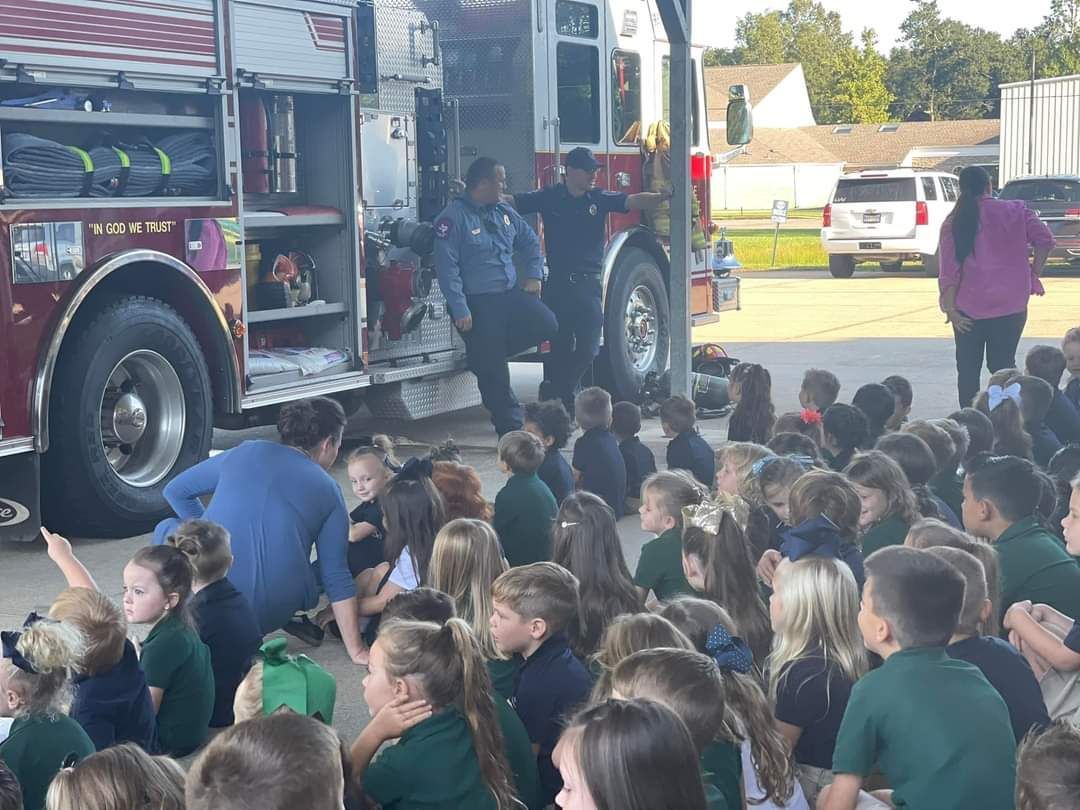 A group of children are sitting in front of a fire truck.