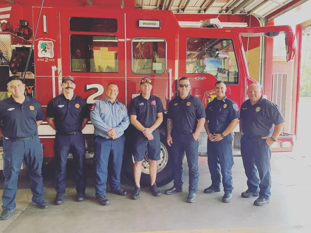 A group of firefighters are posing for a picture in front of a red fire truck.