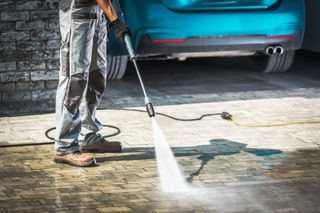 A man is using a high pressure washer to clean a driveway.