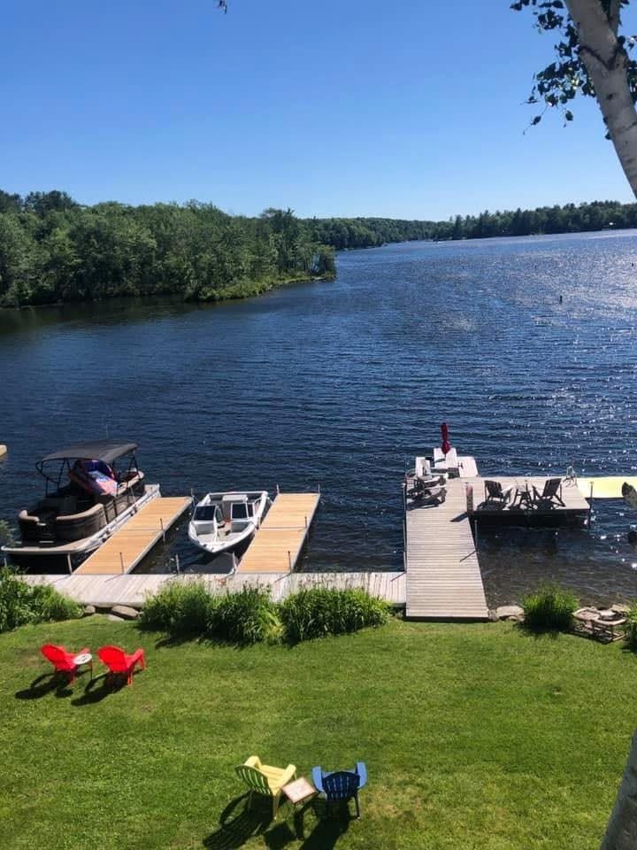 Dock on a sunny lake with boats, green lawn, and red chairs along the shoreline.