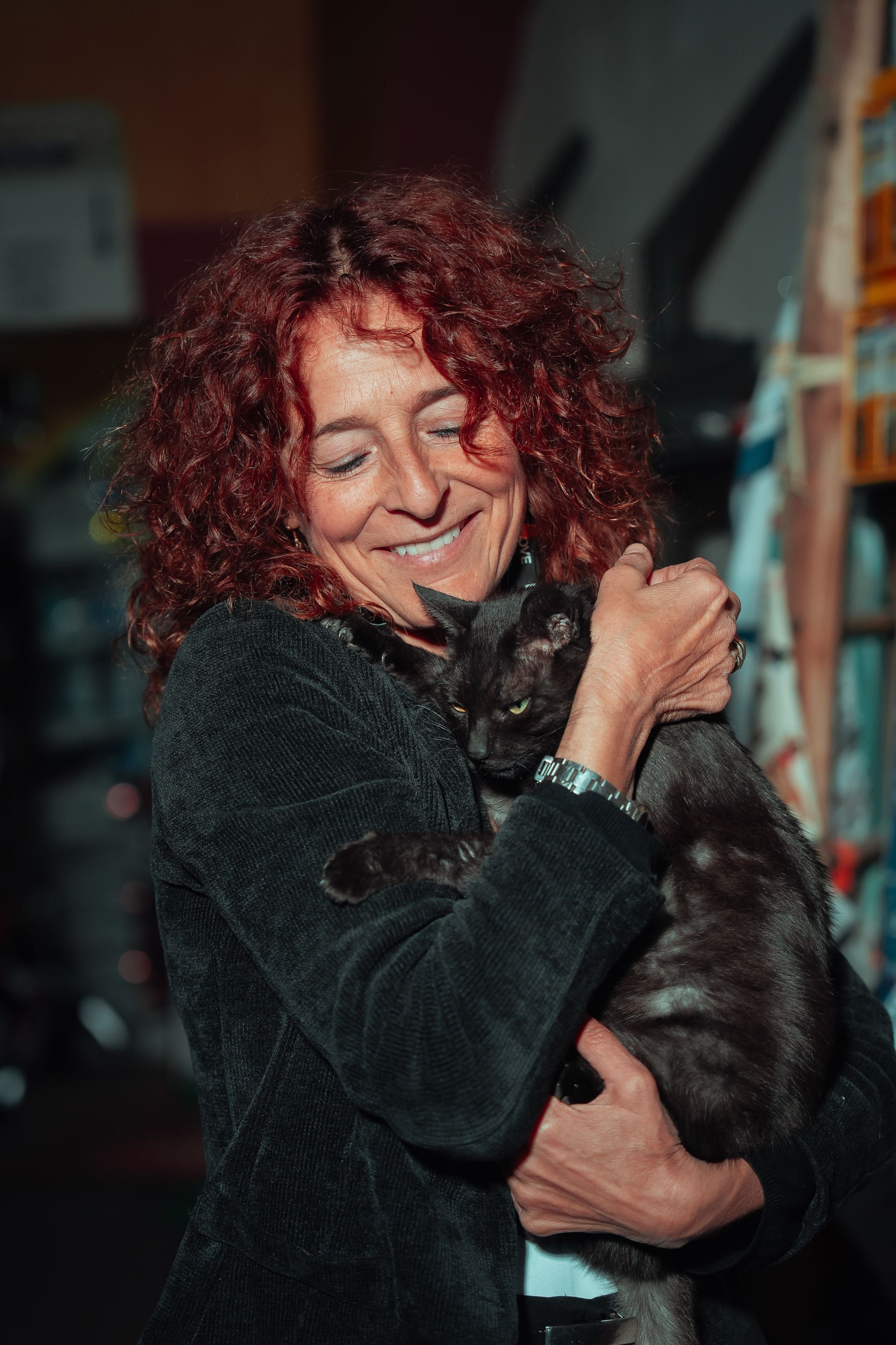 Una donna con i capelli rossi e ricci sorride, tenendo in braccio un gatto nero.