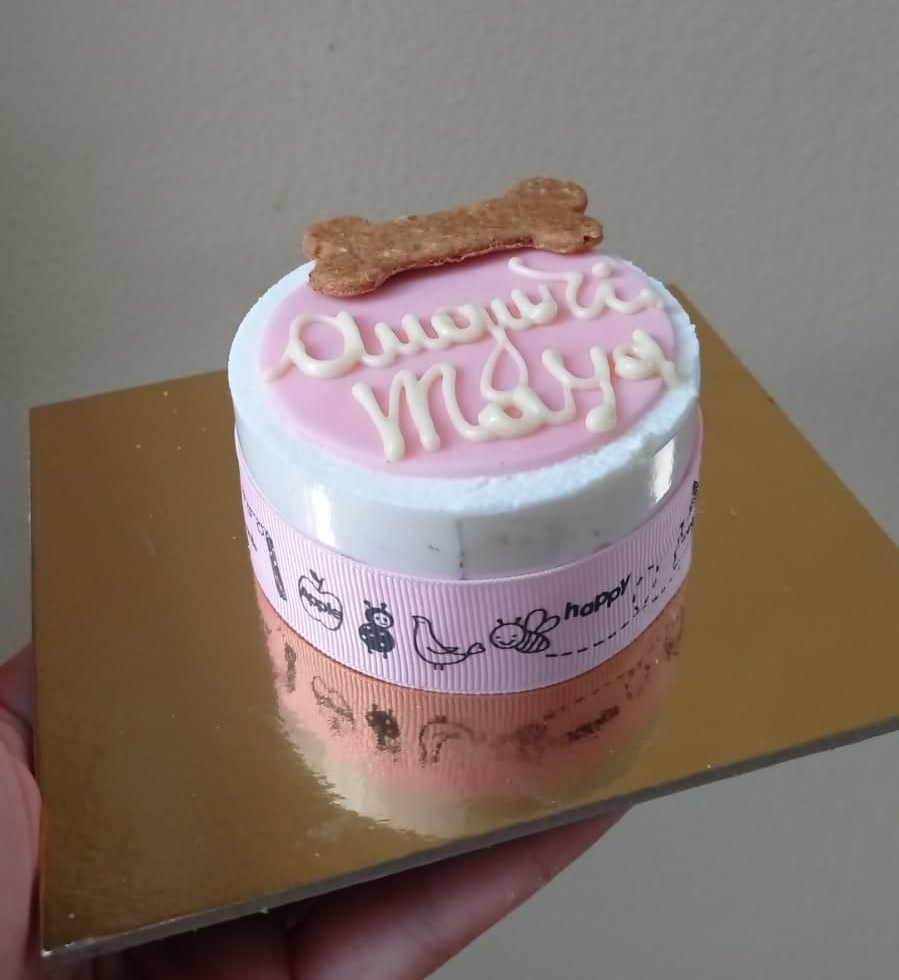 Torta per cani con glassa rosa e dolcetto a forma di osso su un vassoio dorato.