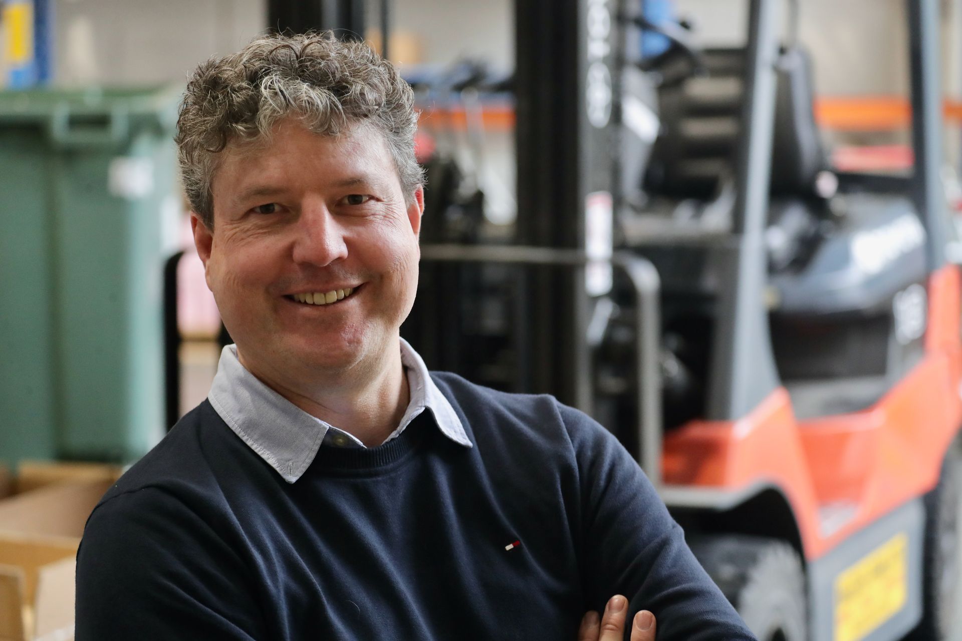 A man with his arms crossed is smiling in front of a forklift.