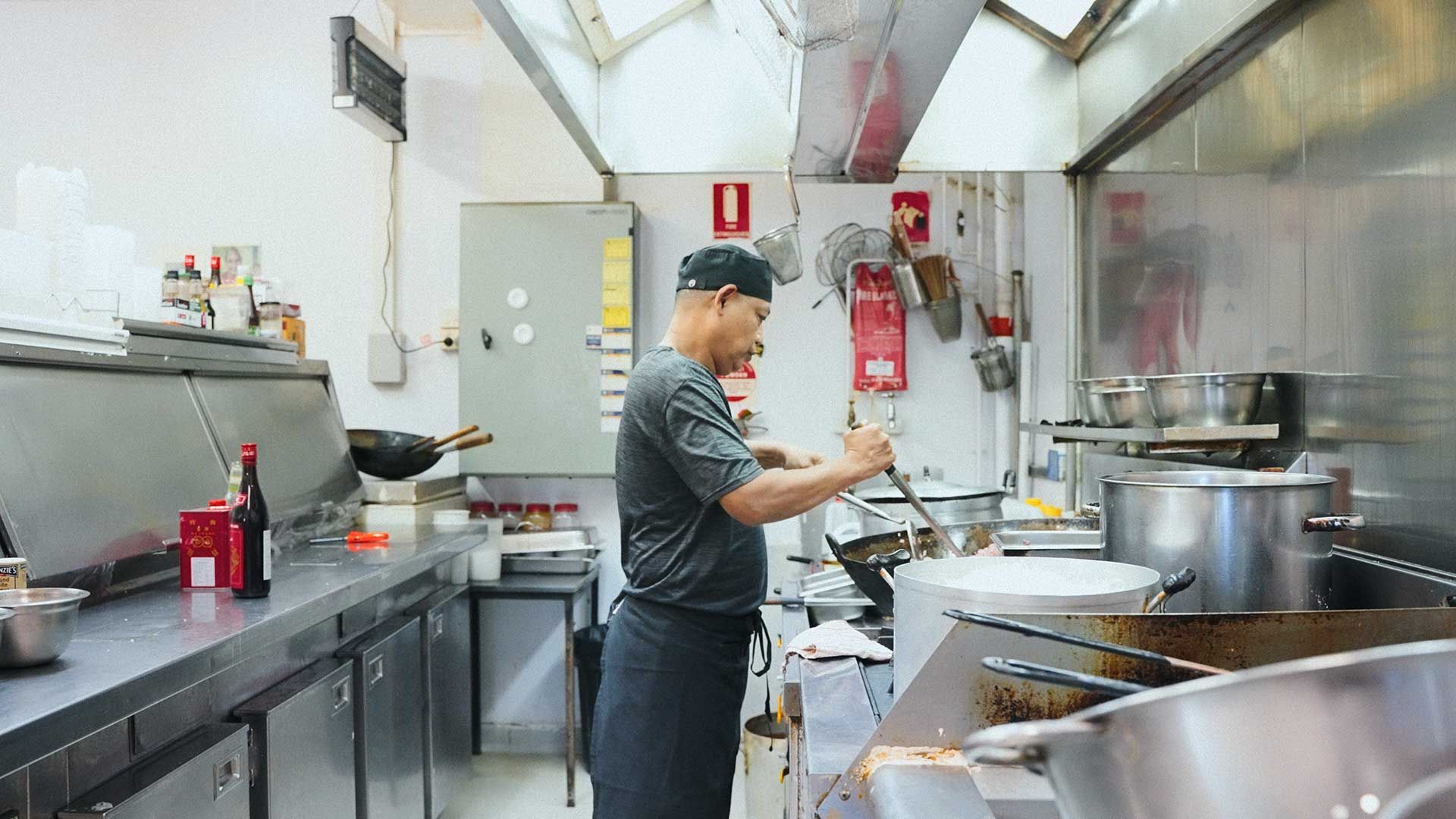 A Man is Standing in a Kitchen Preparing Food — One Thai Cuisine & Noodle Bar In Kirwan, QLD