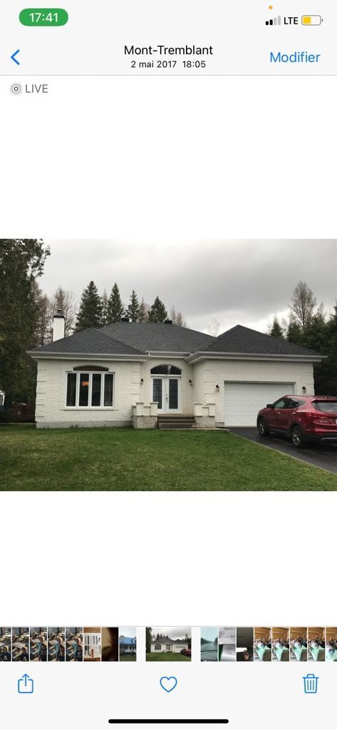 Maison blanche au toit noir, garage et voiture rouge devant. Ciel couvert.