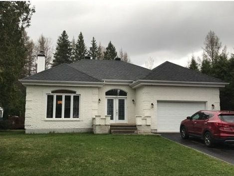 Une maison blanche avec une voiture rouge garée devant.