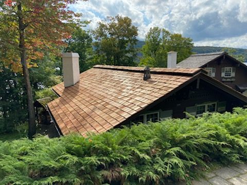 Une maison avec un toit en bois est entourée d'arbres et de buissons.