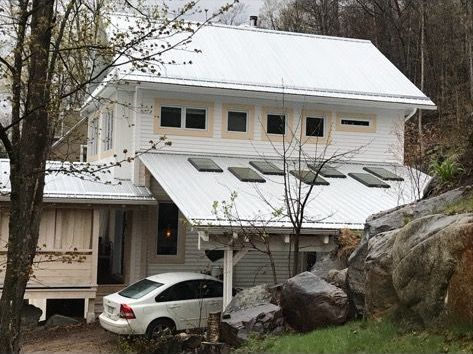 Une voiture blanche est garée devant une maison au toit blanc.