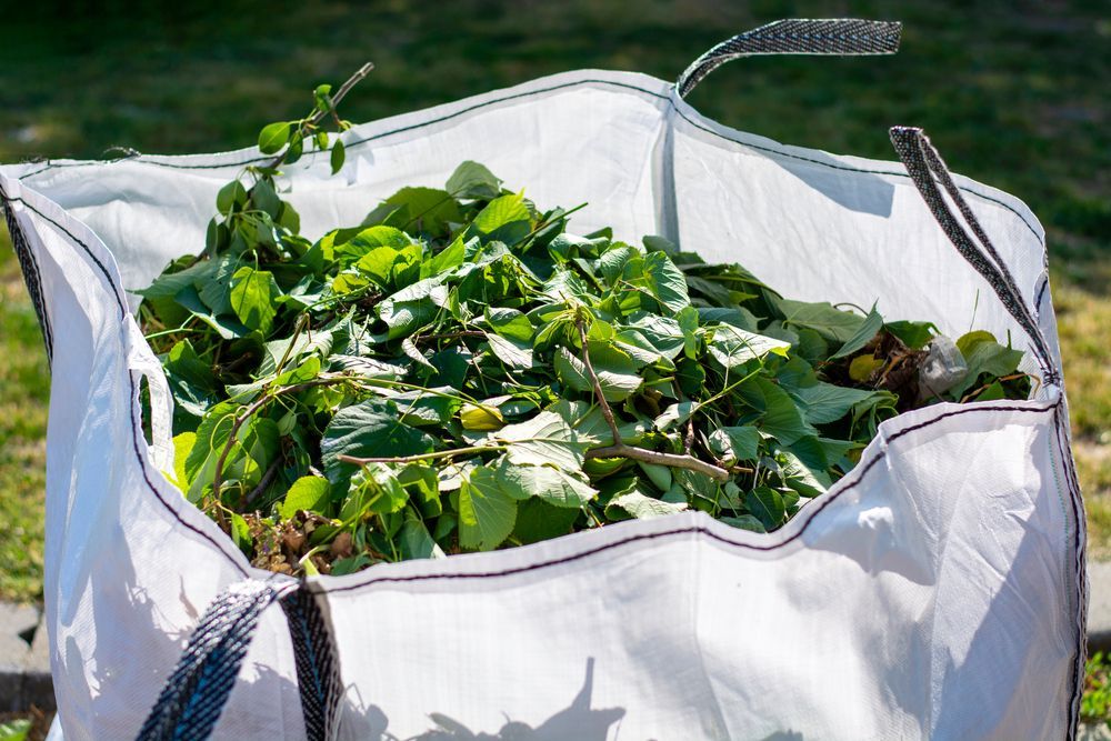 A white bag filled with green leaves and branches — Quality Lawns and Gardens in Raworth, NSW