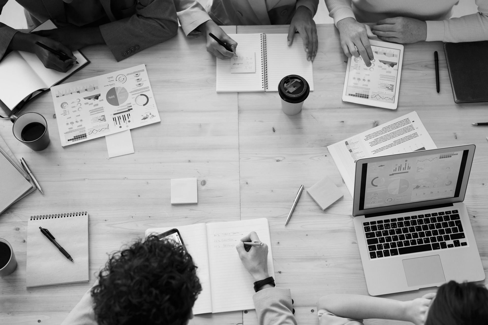 Overhead view of several people at a table, working on papers and a laptop, brainstorming.