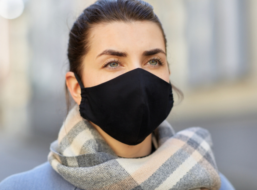 Woman wearing a black face mask and a scarf outside, looking off-camera.