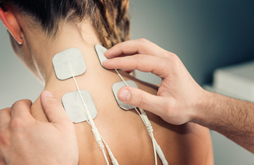 A person receiving electrical stimulation on their back and neck from a physical therapist.