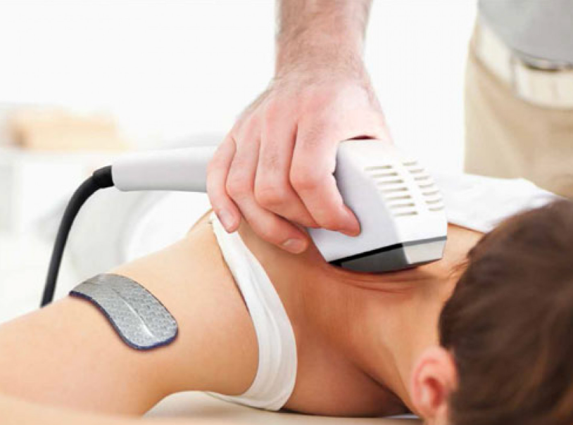 Therapist using a device on a patient's shoulder, with electrode pad in place.