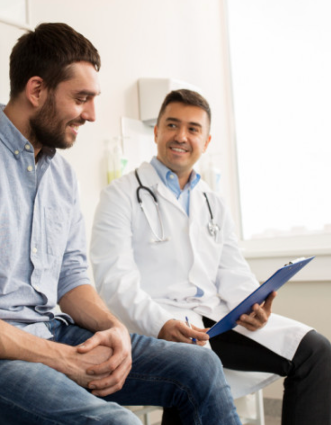Man in light blue shirt smiles at doctor holding clipboard in sunny office.