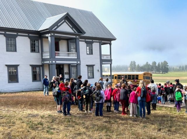 A group of children are standing in front of a large white house.