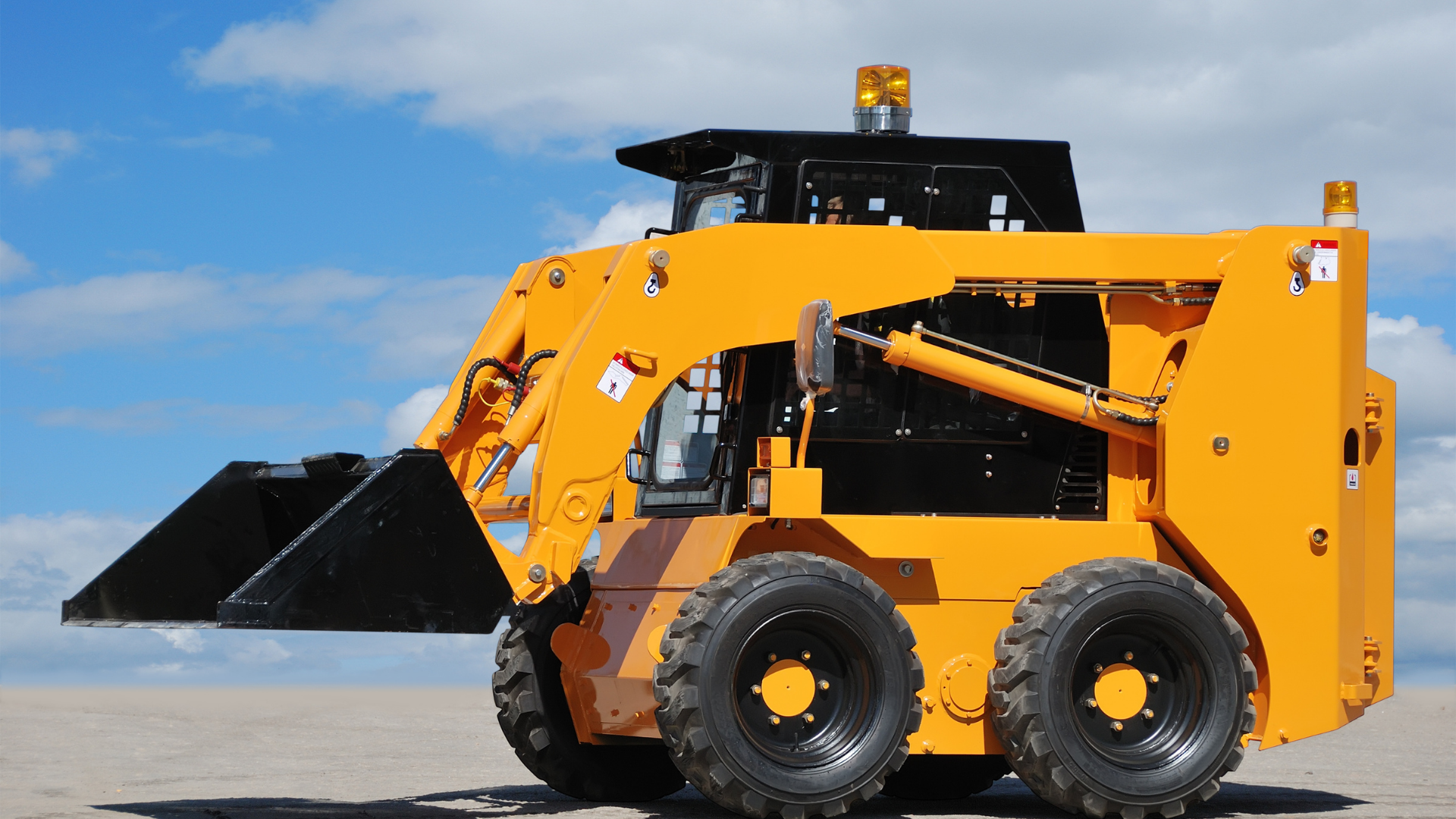 Yellow skid-steer loader with black bucket on a sandy surface under a blue sky