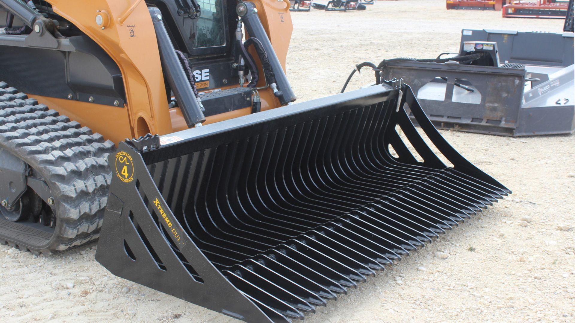 Black skid-steer loader bucket with grapple attachment on gravel lot