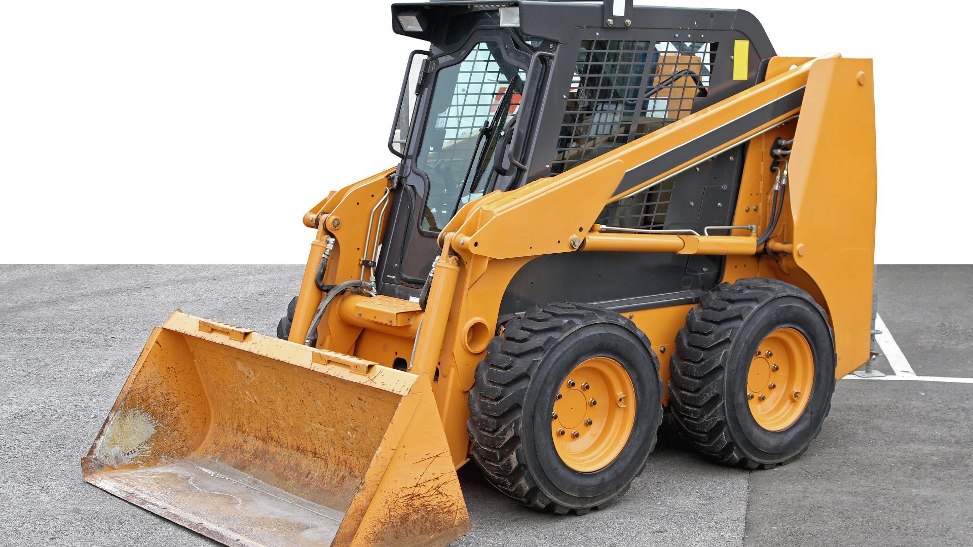 Yellow skid steer loader with front bucket parked on pavement