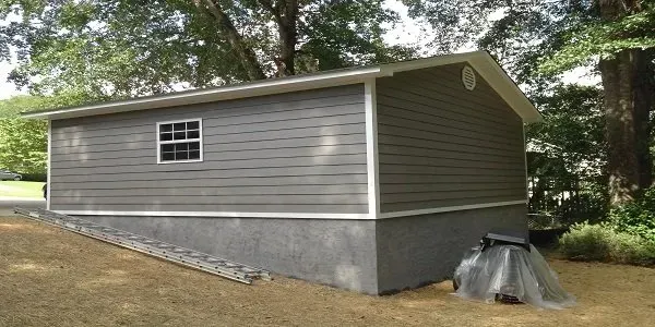 a small gray house with a white roof is sitting on top of a dirt hill .