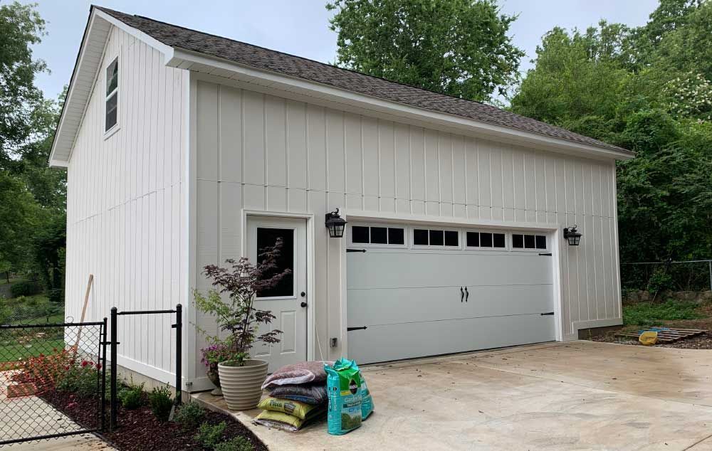 a white garage with two garage doors and a fence in front of it .