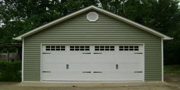 a green garage with white doors and a white roof