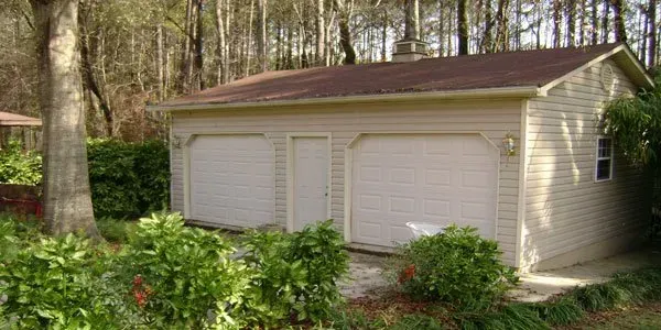 a garage with two garage doors is surrounded by bushes and trees .