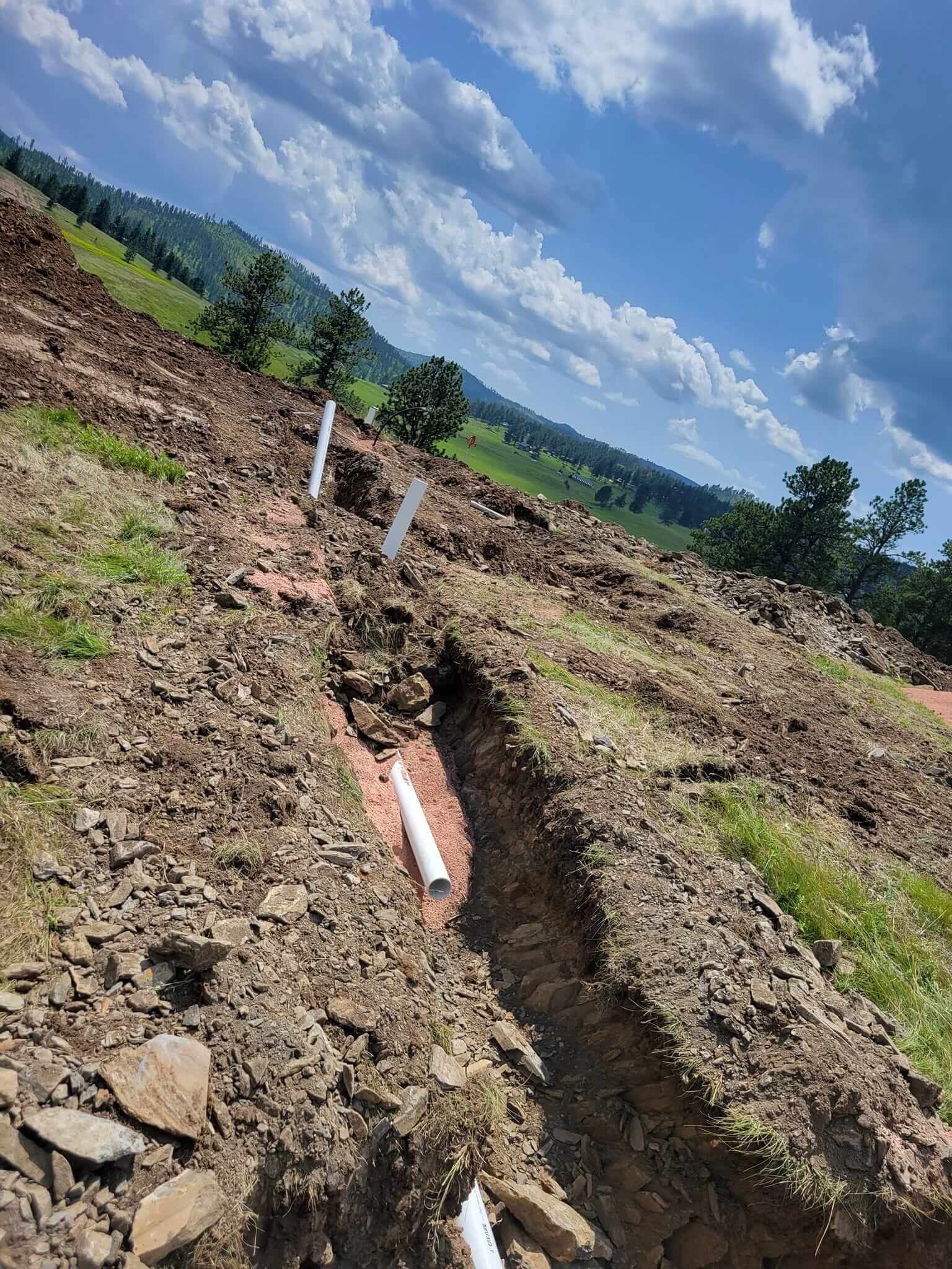 A drain pipe is being installed in the dirt in a field.