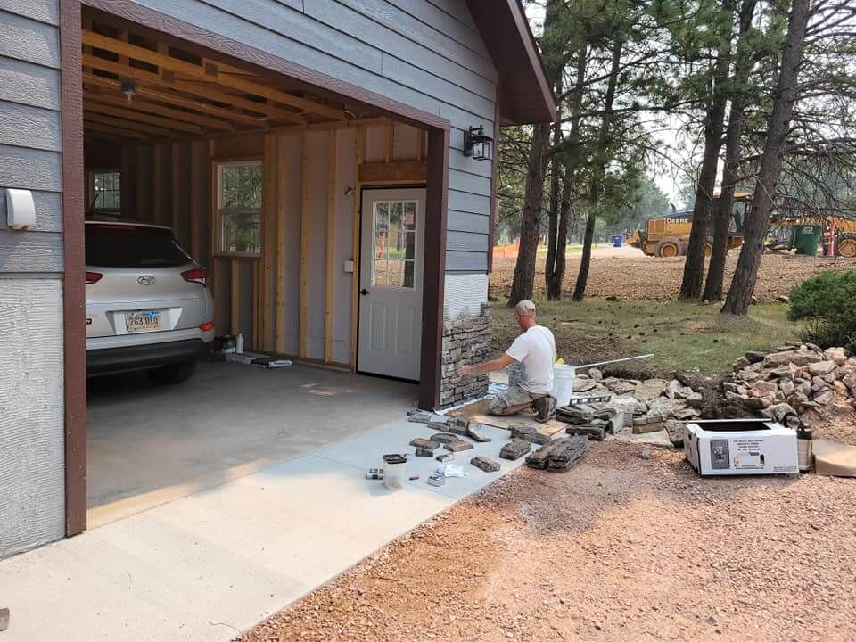 A man is working on a stone wall in front of a garage.