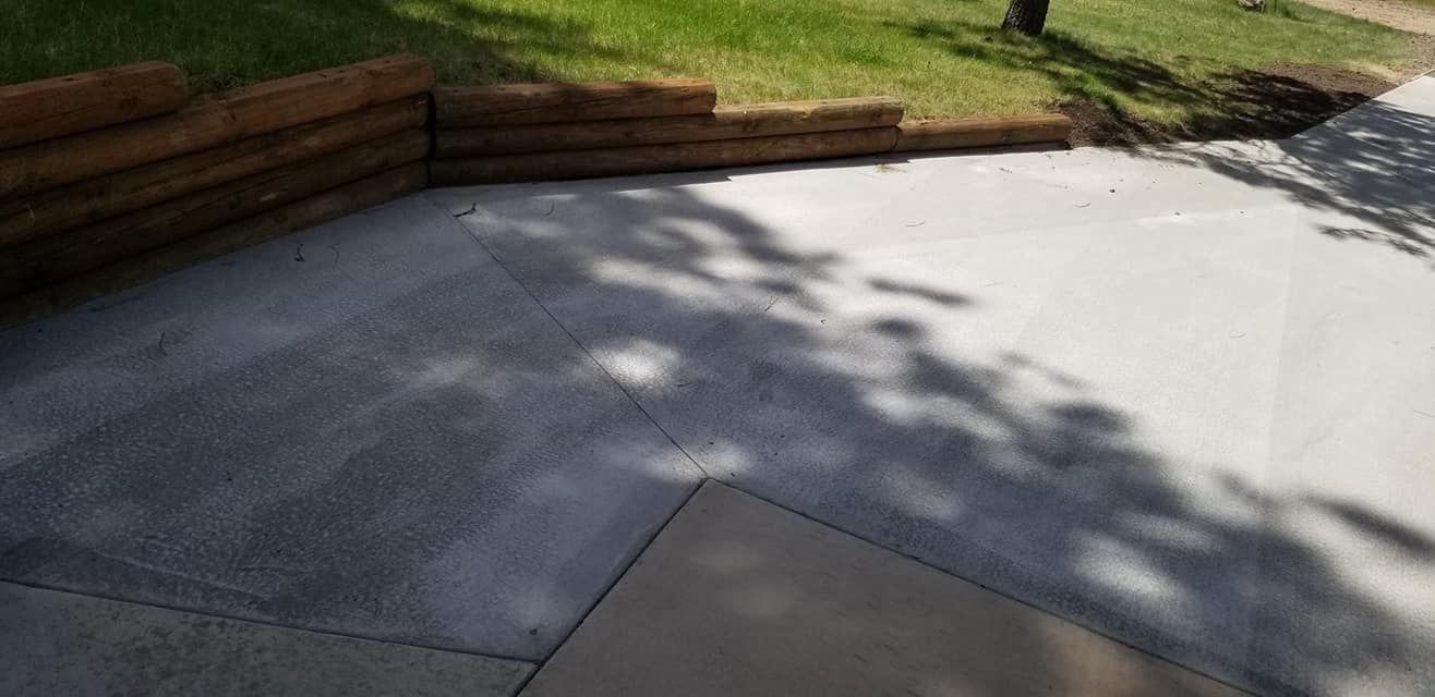 A concrete driveway with a wooden wall and a tree shadow on it.