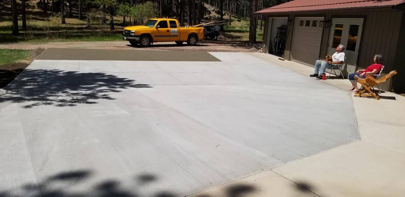 A yellow truck is parked in a driveway next to two men sitting in chairs.