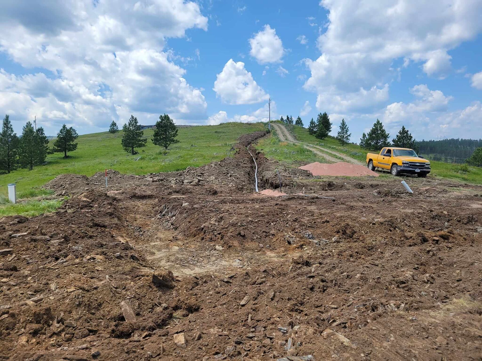 A yellow truck is parked in a dirt field on top of a hill.