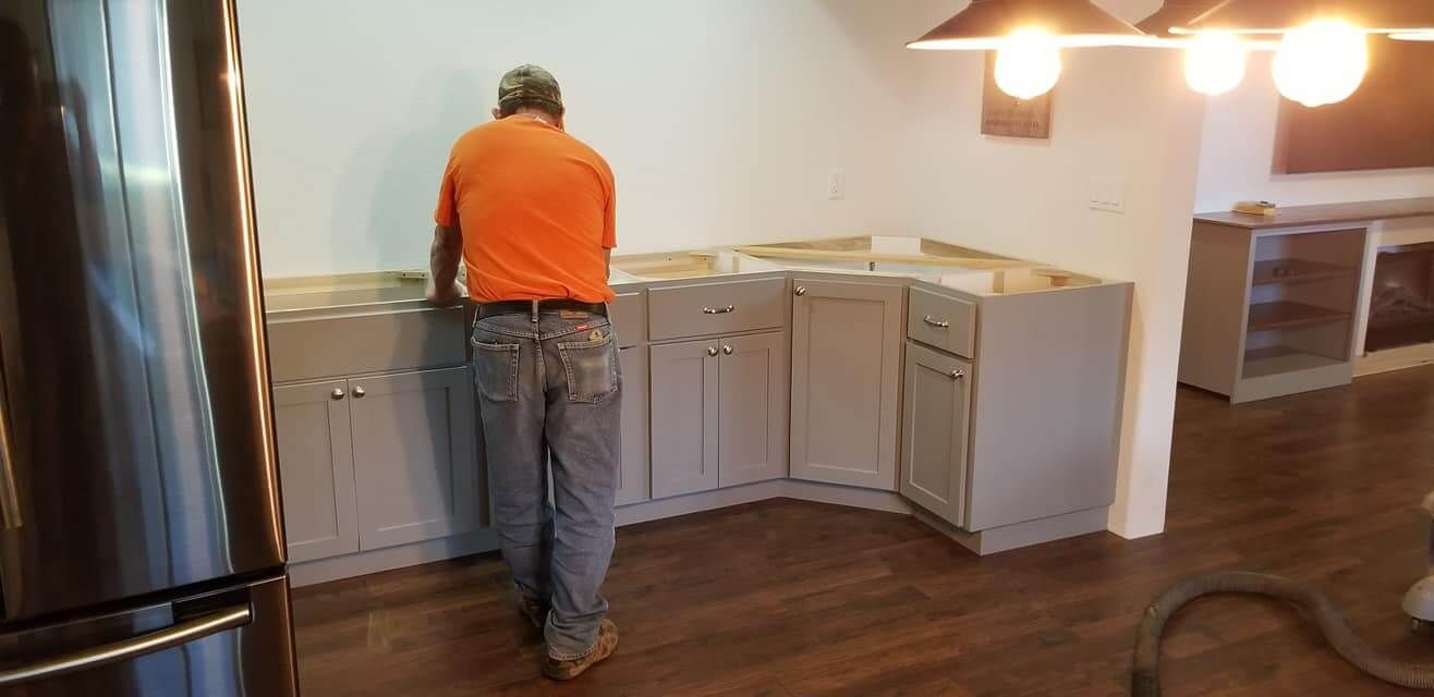 A man in an orange shirt is working on a kitchen counter.