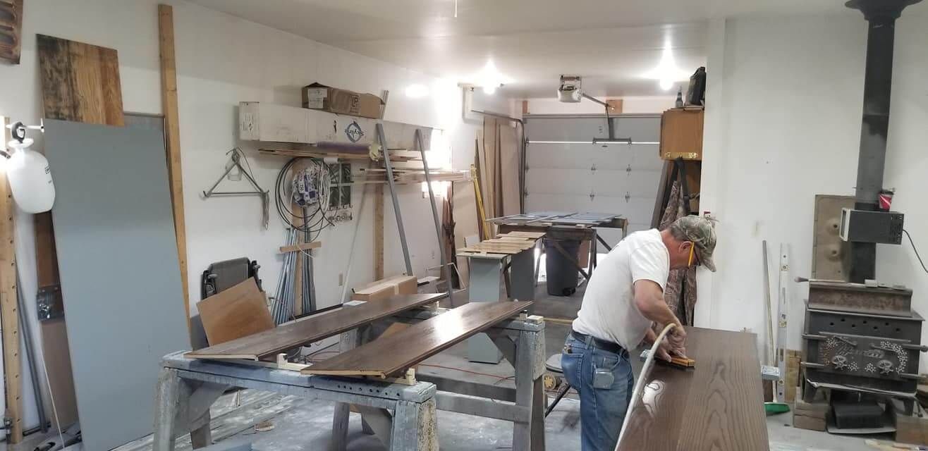 A man is working on a wooden table in a workshop.