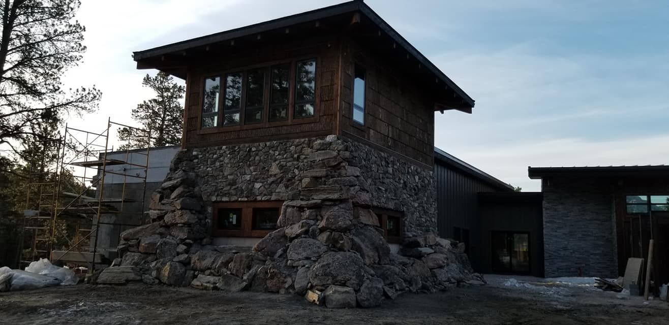 A large stone building with a wooden roof is surrounded by trees.